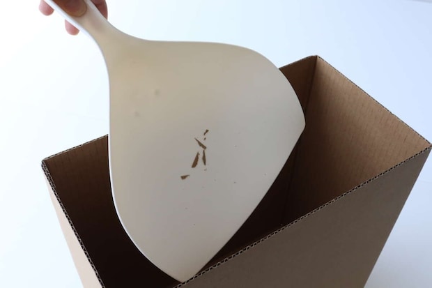 手が、木くずのようなゴミが入ったベージュ色のチリトリを段ボール箱のゴミ箱に捨てようとしている。 手が、木くずのようなゴミが入ったベージュ色のチリトリを段ボール箱のゴミ箱に捨てようとしている。