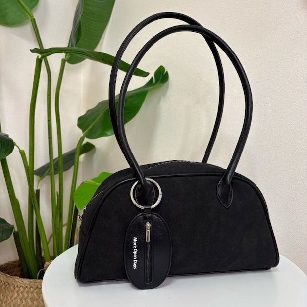 黒い丸みのあるフォルムのハンドバッグとチャーム、観葉植物