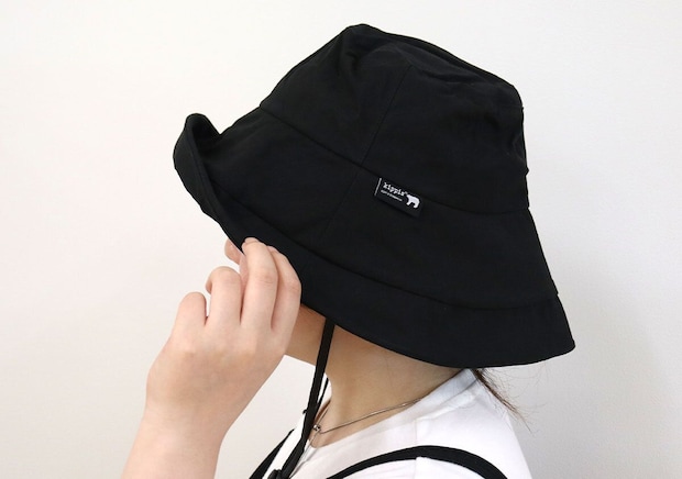 黒いUVハットをかぶった女性が、つばの形を整えている横顔