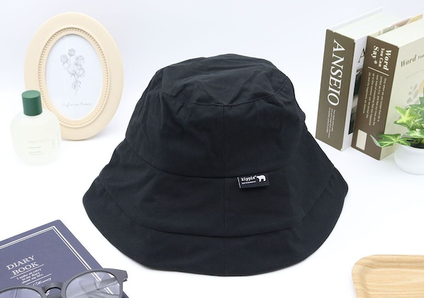 黒いkippisのつば広UVハットが置かれ、背景に本や小物が写っている 黒いkippisのつば広UVハットが置かれ、背景に本や小物が写っている