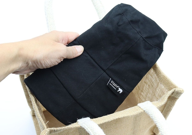 折りたたんだ黒いUVハットを麻のトートバッグに入れている手元