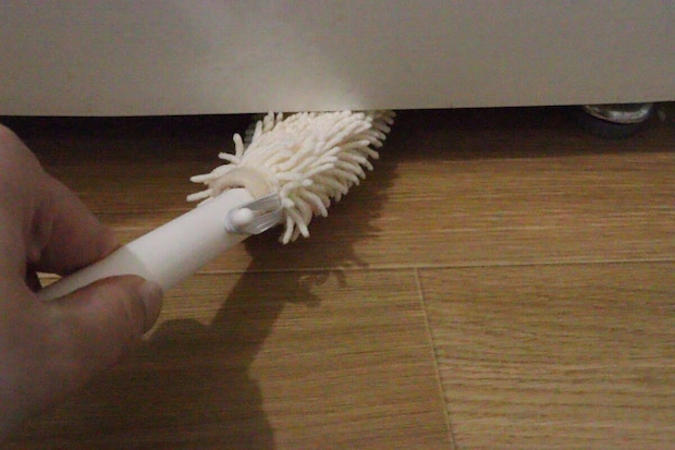 冷蔵庫の下の狭い隙間をハンディモップで掃除する手元