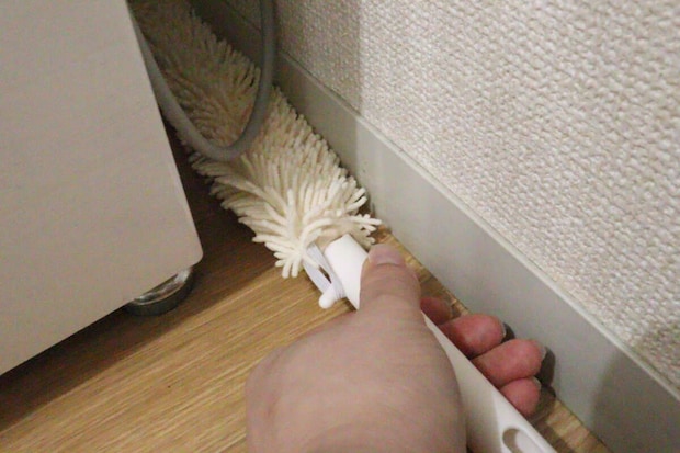 家具と壁の間の狭い隙間をハンディモップで掃除する手元