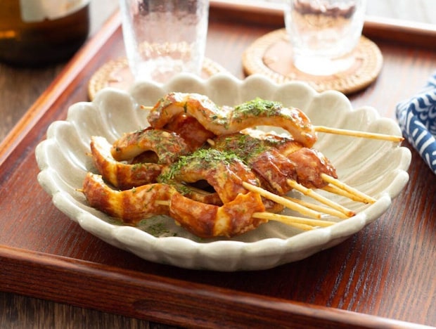 マヨソースで炒めたちくわを串に刺し青のりをかけた料理が花形の白い皿に盛られている マヨソースで炒めたちくわを串に刺し青のりをかけた料理が花形の白い皿に盛られている