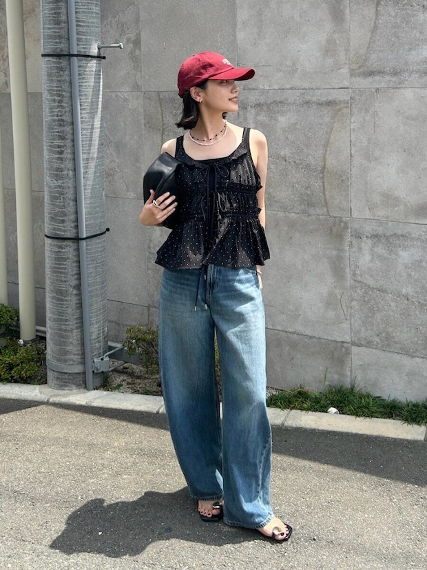 赤いキャップと黒いドット柄キャミソール、ワイドデニムを着用した女性がバッグを持ち横を向いて立っている 赤いキャップと黒いドット柄キャミソール、ワイドデニムを着用した女性がバッグを持ち横を向いて立っている