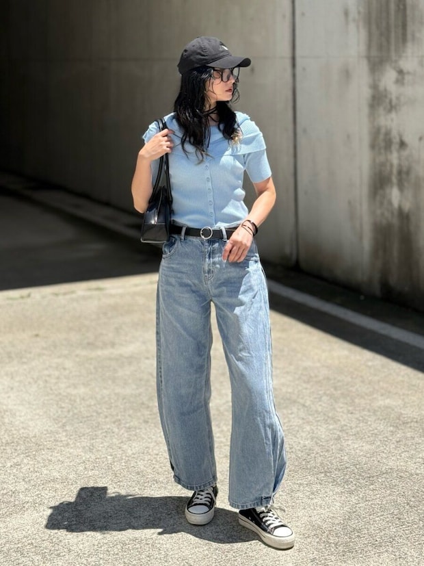 黒いキャップと水色のカーディガン、ライトブルーのワイドデニムを着用した女性が横を向いて立っている 黒いキャップと水色のカーディガン、ライトブルーのワイドデニムを着用した女性が横を向いて立っている