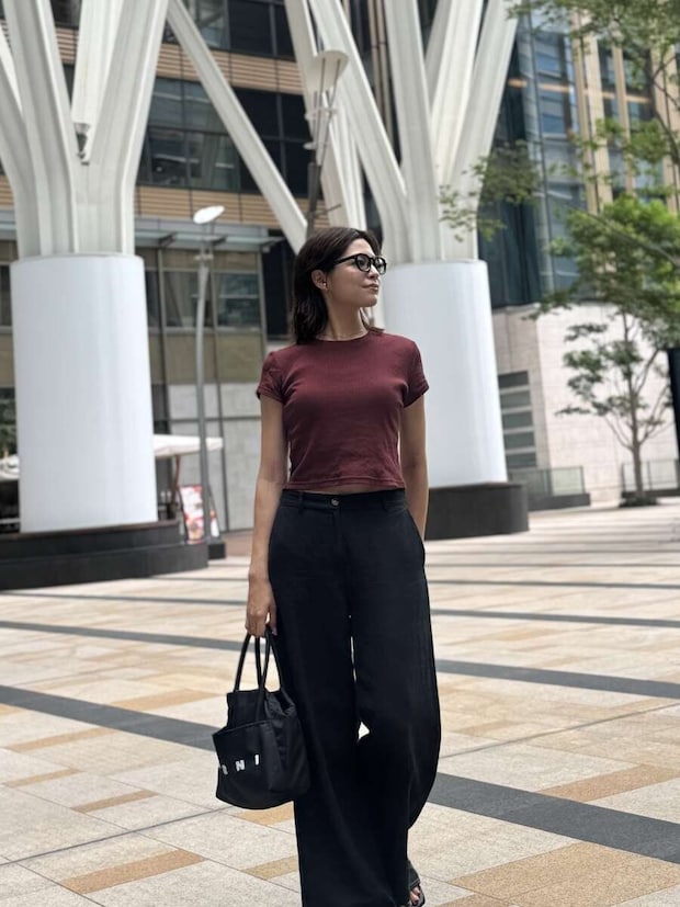 赤茶色のミニTと黒いワイドパンツを着用した女性が、街中でバッグを持って立っている 赤茶色のミニTと黒いワイドパンツを着用した女性が、街中でバッグを持って立っている
