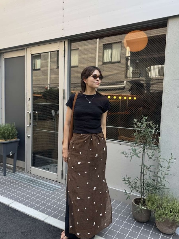 黒いミニTとブラウンのロングスカートを着用した女性が、店の前で立っている 黒いミニTとブラウンのロングスカートを着用した女性が、店の前で立っている