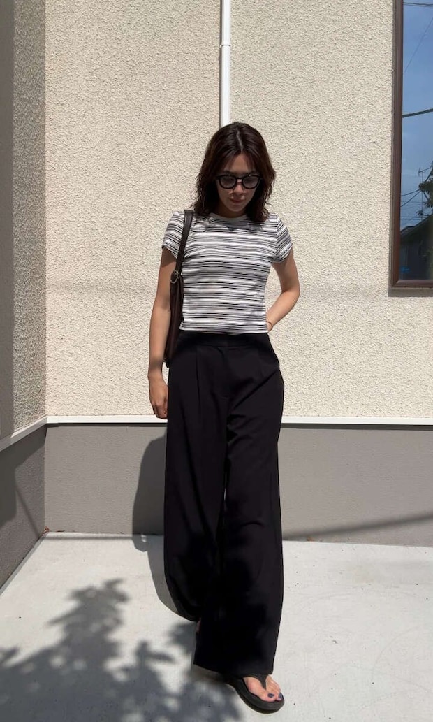 ボーダー柄のミニTと黒いワイドパンツを着用し、サングラスをかけた女性が立っている ボーダー柄のミニTと黒いワイドパンツを着用し、サングラスをかけた女性が立っている