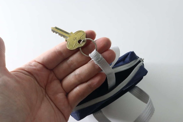 手がポーチのキーリングに鍵を取り付けている様子