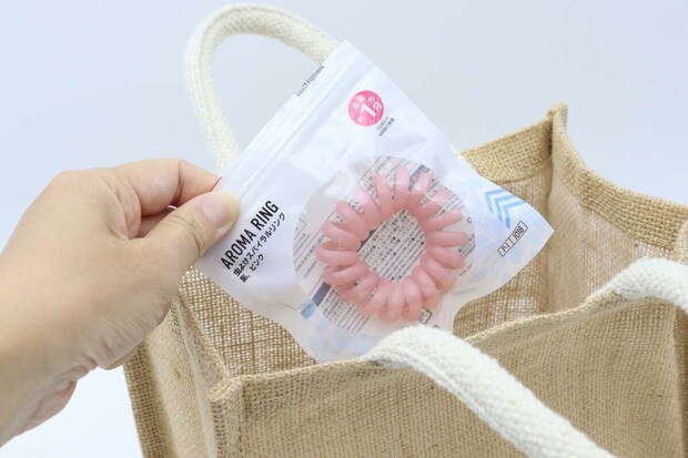 ジュート素材のバッグにダイソー虫よけスパイラルリングのパッケージを入れる手。