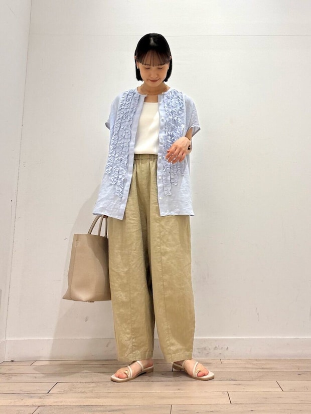 フリル付きブルーシャツとベージュワイドパンツの女性がバッグを持つ フリル付きブルーシャツとベージュワイドパンツの女性がバッグを持つ