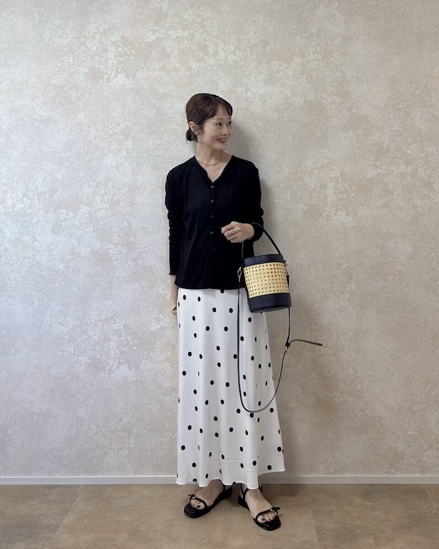 GU サテンドットフレアスカート 白のドット柄スカートと黒いカーディガンを着た女性が斜めを向いて立っている