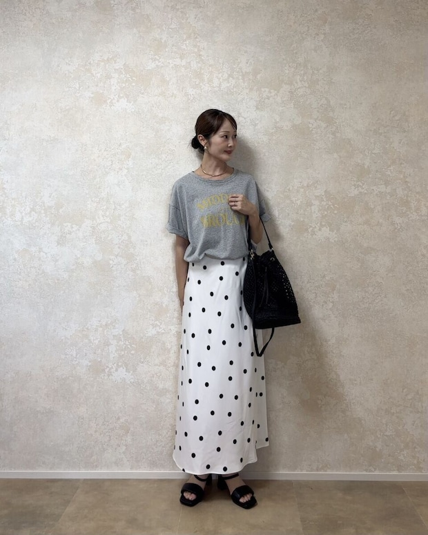 GU サテンドットフレアスカート 白のドット柄スカートとグレーのロゴTシャツを着た女性が斜めを向いて立っている