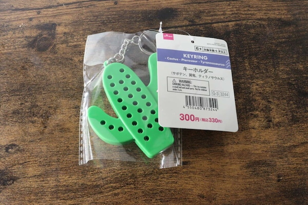 透明な袋に入った緑色のサボテン型キーホルダーと商品タグが木目のテーブルに置かれている