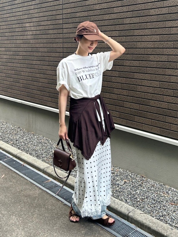 白のロゴTにドット柄スカートとデニムを重ね、茶色のキャップを被る女性 白のロゴTにドット柄スカートとデニムを重ね、茶色のキャップを被る女性