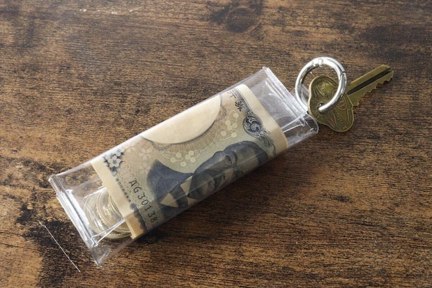 PVCコインポーチに硬貨と千円札、鍵がリングに取り付けられて木目のテーブルに置かれている