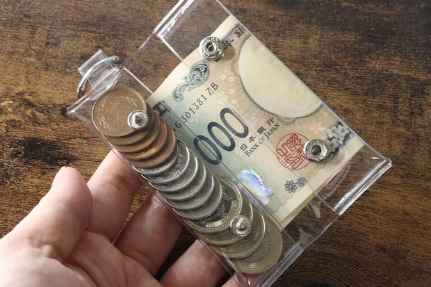 手がPVCコインポーチを持ち、中に硬貨と二つ折りの千円札が入っている