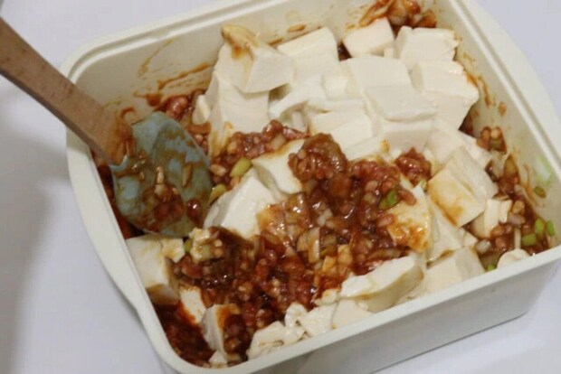 四角い容器の中で豆腐と麻婆豆腐の素を木製スプーンで混ぜている