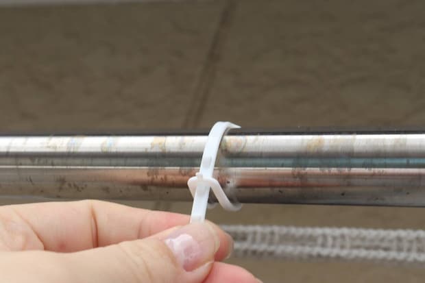 物干し竿に白いピンチの紐を結びつける手元