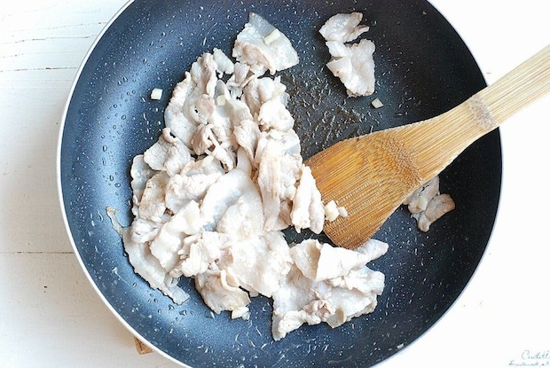 フライパンで白っぽくなるまで炒められている豚バラ肉と木製のへら フライパンで白っぽくなるまで炒められている豚バラ肉と木製のへら