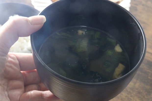 女性が味噌汁の入ったこげ茶色の汁椀を持つ 女性が味噌汁の入ったこげ茶色の汁椀を持つ