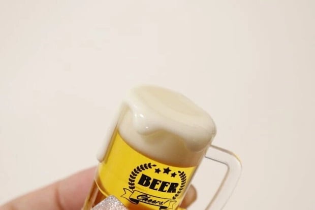 女性がビールジョッキ型キーホルダーを持ち、泡の質感を強調