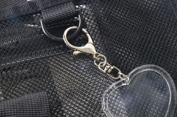 メッシュバッグのDカンにハート型の透明なキーホルダーが取り付けられている。 メッシュバッグのDカンにハート型の透明なキーホルダーが取り付けられている。