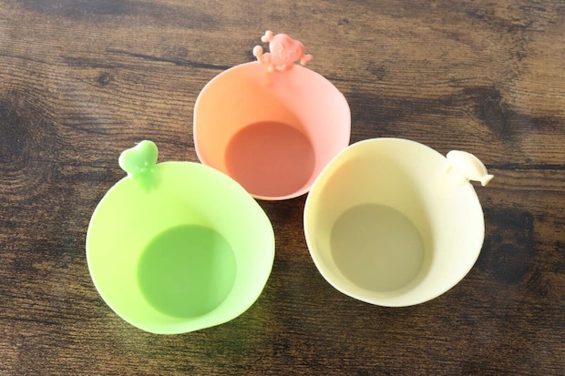 ピンク、緑、黄色のシリコンおかずカップ3つが木目のテーブルに並べられている