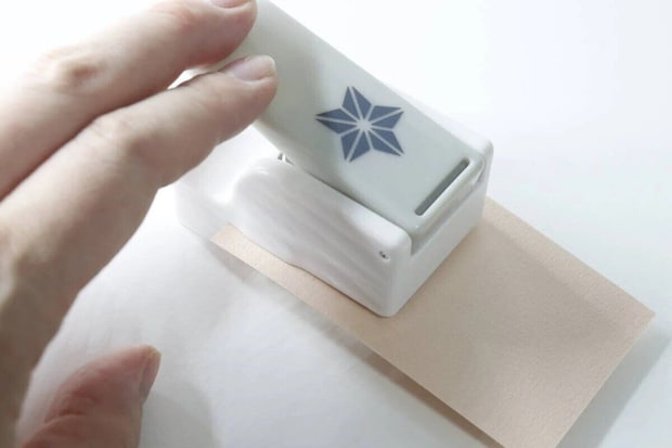 右手がクラフトパンチでベージュの紙をエンボス加工している様子