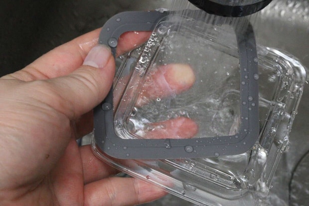 女性の手が持っている密閉容器のフタに、シャワーから水が勢いよくかかっている様子