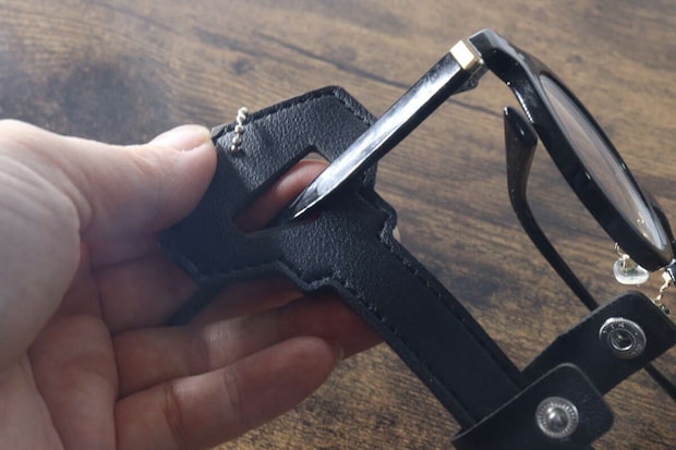 手が黒縁メガネのテンプルを鍵型メガネホルダーの上部ホールに通している 手が黒縁メガネのテンプルを鍵型メガネホルダーの上部ホールに通している