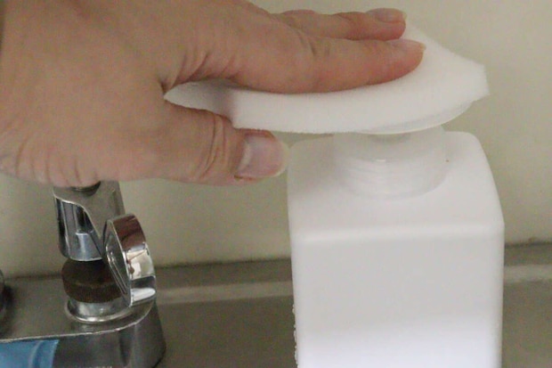 スポンジでワンプッシュディスペンサーのポンプを押す手元 スポンジでワンプッシュディスペンサーのポンプを押す手元