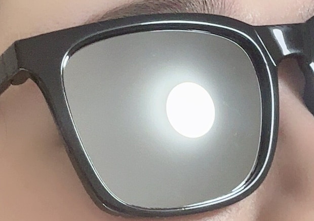 黒いウェリントン型サングラスをかけた人の目元に太陽の光が反射しているアップ