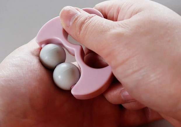 女性がピンク色のミニ携帯フェイスローラーを手に持ち使用している