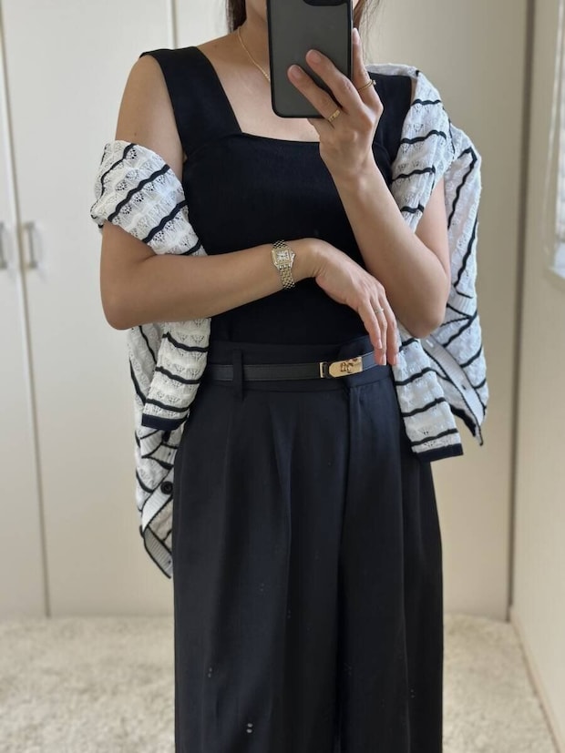 黒いニットインナーとワイドパンツにボーダーカーディガンを肩掛けしスマホを持つ女性