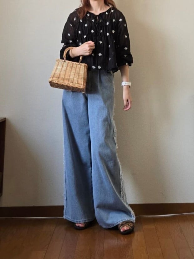 花柄黒ブラウスとライトブルーのワイドデニム、カゴバッグを持つ女性