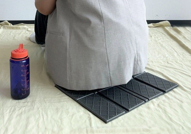 8つ折りレジャーマットに座る人の下半身と水筒が写っている