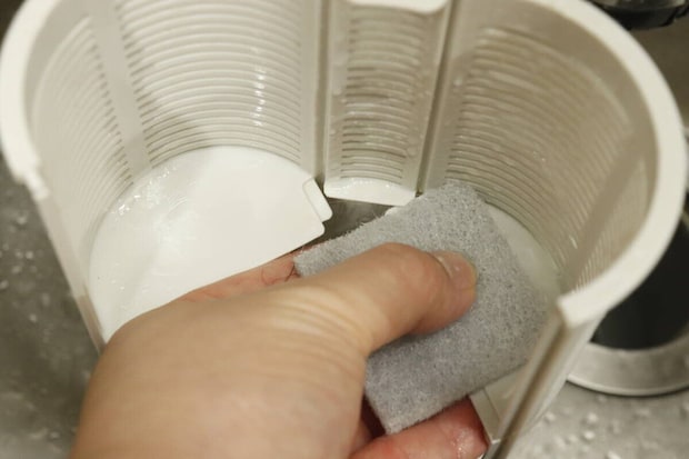 排水溝の白いプラスチック製パーツをスポンジで洗っている