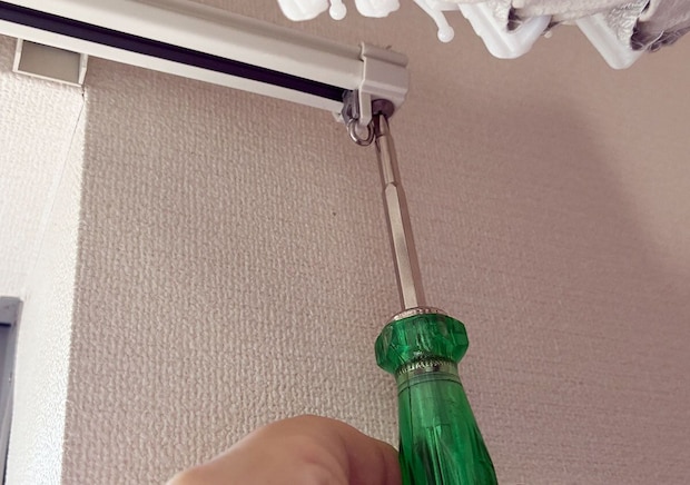 緑色のドライバーを使ってカーテンレールのキャップストップを外している手元 緑色のドライバーを使ってカーテンレールのキャップストップを外している手元