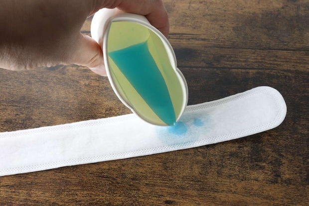青い液体を計量カップから白い汗取りパットに注いでいる 青い液体を計量カップから白い汗取りパットに注いでいる