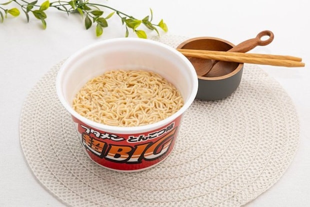 ブタメン超BIGの麺が見えるカップ麺が白い敷物の上に置かれている ブタメン超BIGの麺が見えるカップ麺が白い敷物の上に置かれている