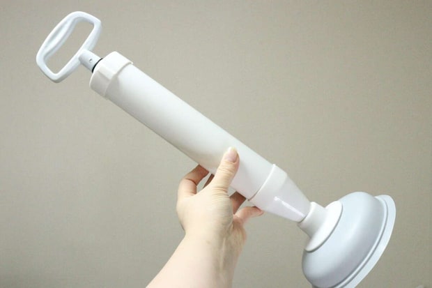 女性が白いトイレ用パイプクリーナーを手に持ち上げている