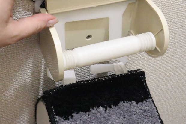 女性の手が古い蛇腹タイプのトイレットペーパーホルダーを外している