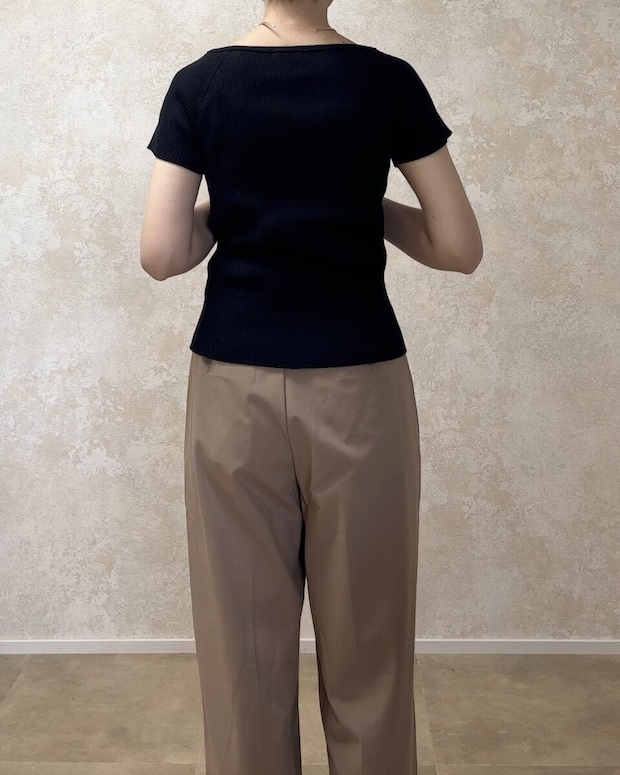 黒いリブカーディガンとベージュのワイドパンツを着用した女性が後ろ向きに立っている