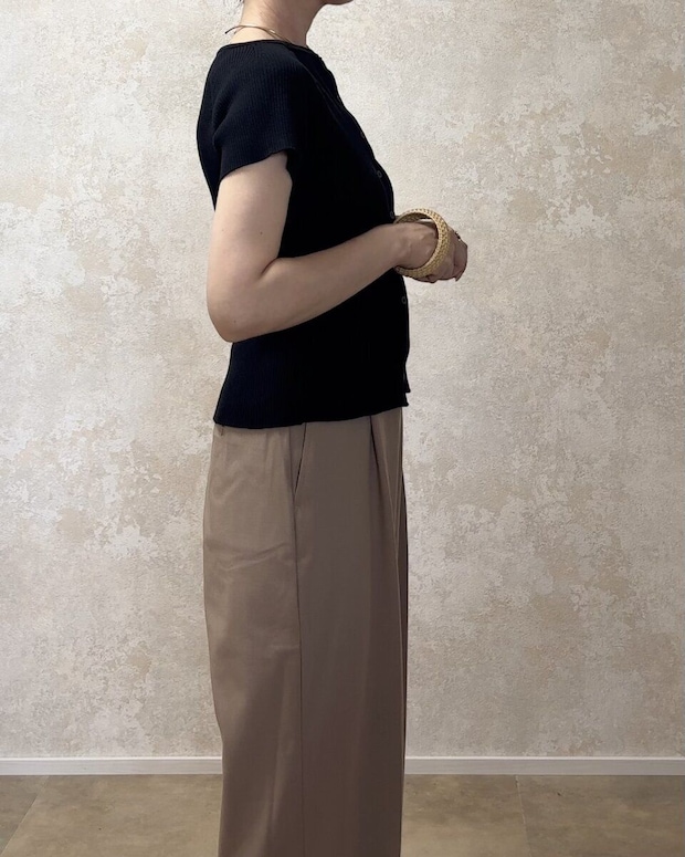 黒いリブカーディガンとベージュのワイドパンツを着用した女性が横向きに立っている