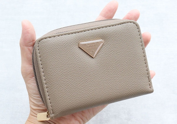 手のひらに乗せた茶色のミニ財布。正面のロゴプレートが特徴。
