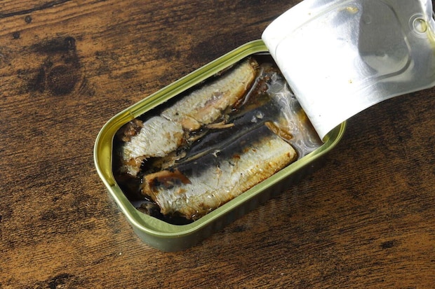 開封された「いわしオイル漬け」の缶詰が木目のテーブルに置かれ、中にはオイルに浸かったいわしが数尾見える