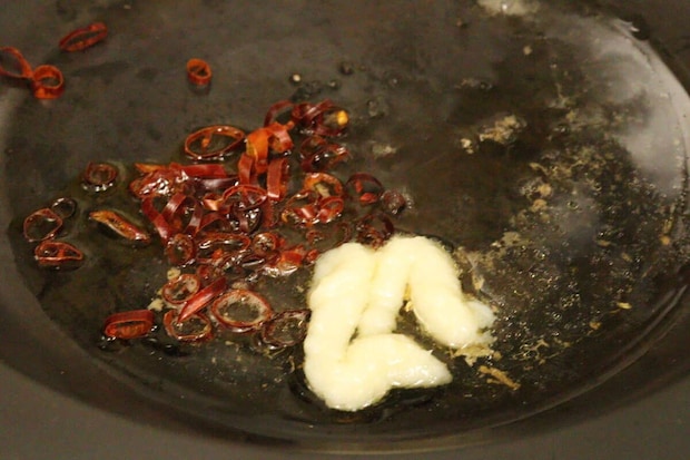 フライパンにいわし缶のオイル、にんにくチューブ、輪切り唐辛子が入っており、加熱されている様子