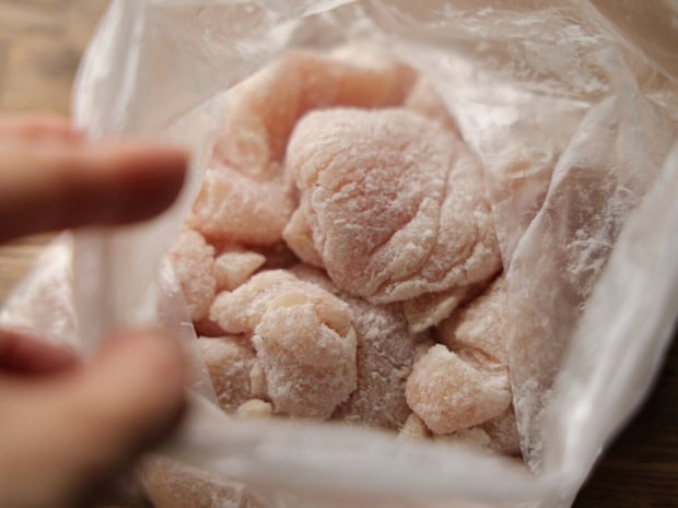 ビニール袋の中で片栗粉がまぶされた鶏むね肉のそぎ切りを指で示している様子 ビニール袋の中で片栗粉がまぶされた鶏むね肉のそぎ切りを指で示している様子